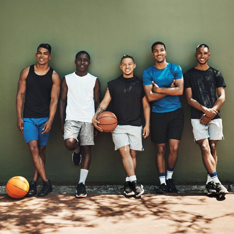 Five men posing outdoors with a basketball against a green wall.